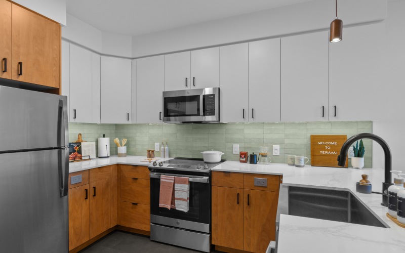 Staged kitchen featuring custom backsplash, quartz countertops, stainless steel appliances, and dual tone cabinets